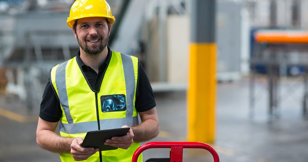 Trabalhador com capacete amarelo e tablet durante exame ocupacional